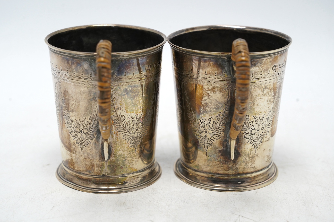 A pair of George V engraved silver mugs, with rattan handles, William Aitken, Birmingham, 1920, height 95mm, gross weight 5.9oz. Condition - fair